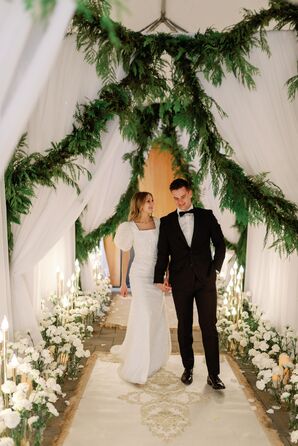 Groom in Tuxedo, Bride in Puff-Sleeved Gown Walk Under Draping, Hanging Greenery Entrance