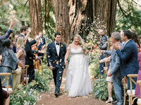 A happy couple walk back down the aisle, beaming, with their friends and towering redwoods in the background.