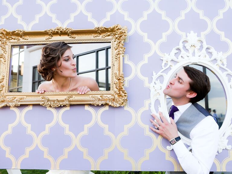 Couple poses in picture frame props for a wedding photo booth. 