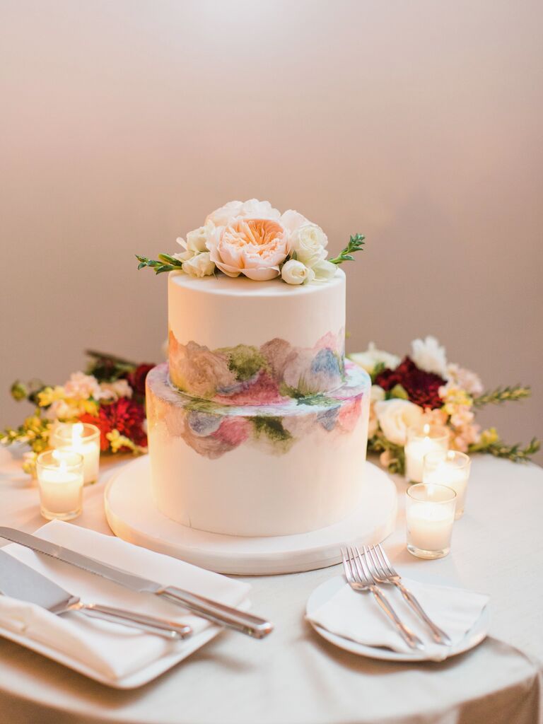 white two tier wedding cake with pastel watercolor shapes and fresh roses on top