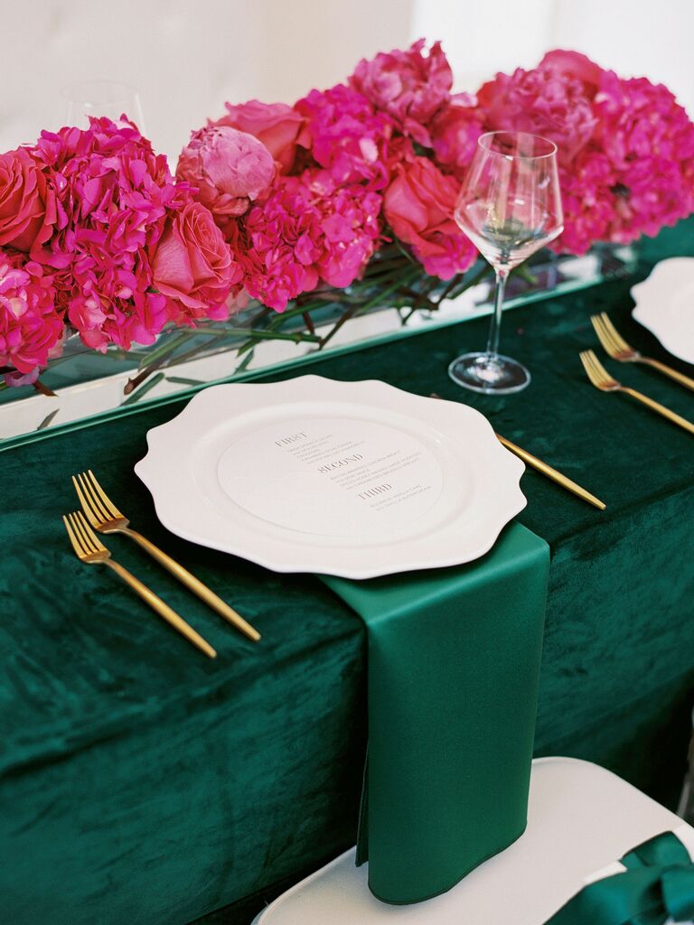 wedding table with emerald green velvet tablecloth, magenta flower table runner and gold flatware