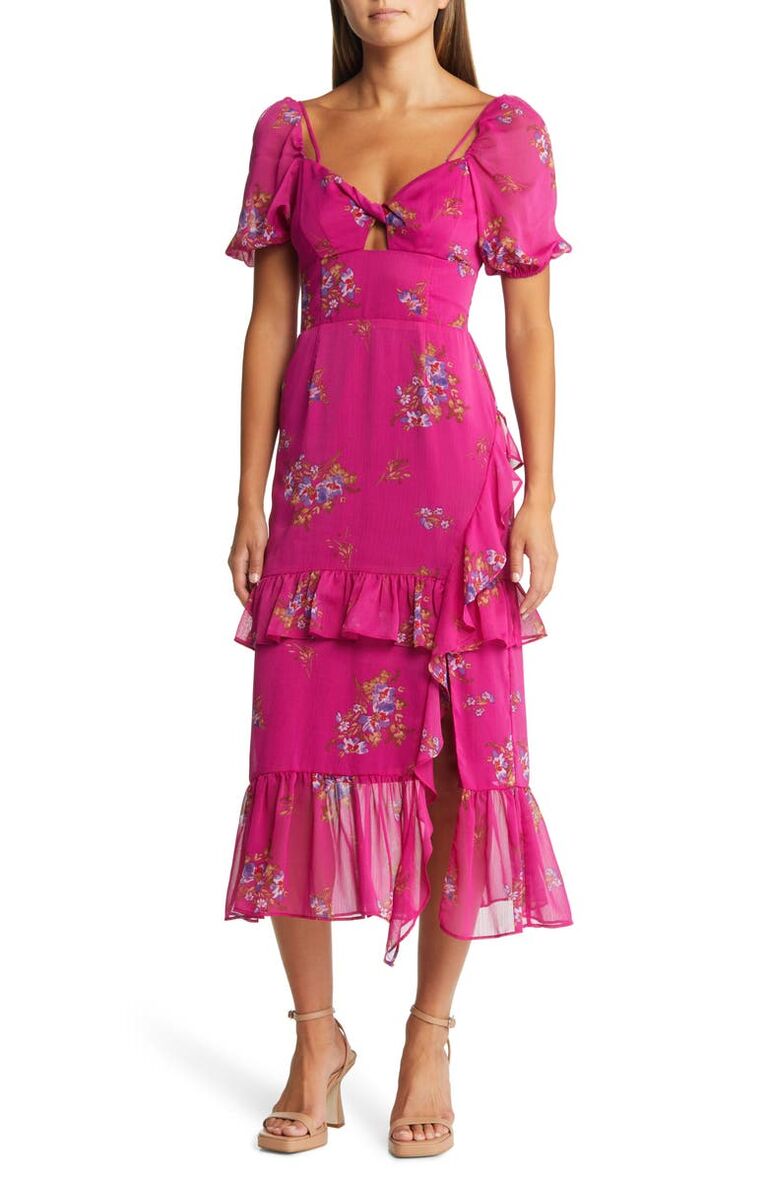 Model wears a mid-length deep pink dresses with a floral print and ruffled hem.