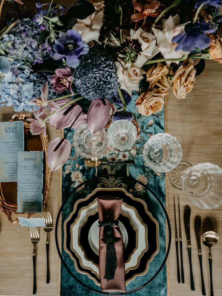 2023 wedding flower trend moody tablescape with embroidered table runner and matching centerpiece with purple and blue flowers