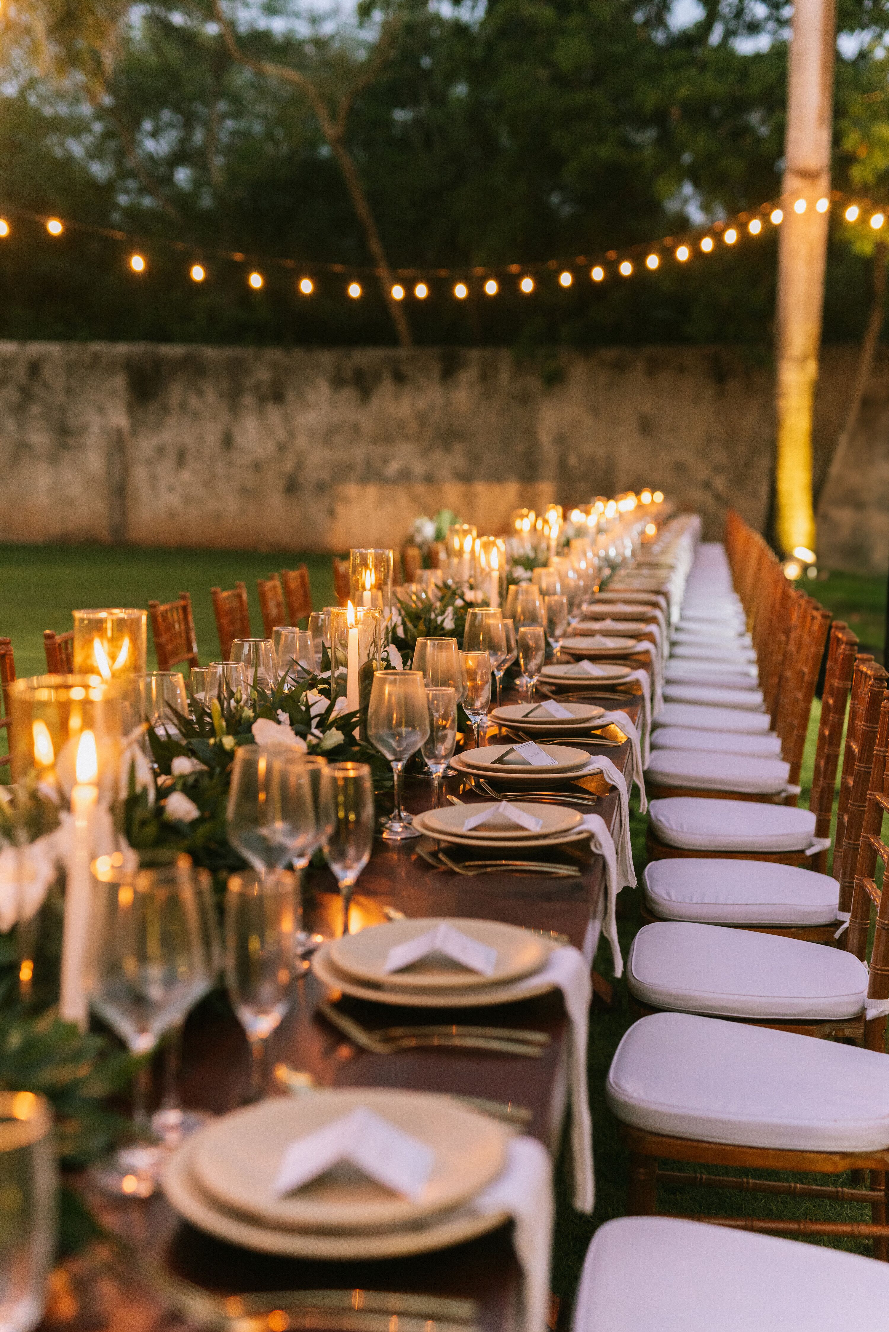 Long Minimalistic Dining Table, Greenery Runner and Taper Candles Under String Lights