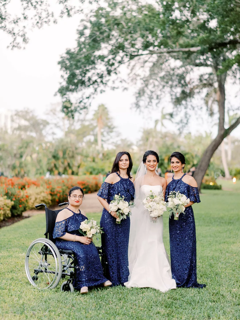 A bride poses with her three bridesmaids, each of whom wears sparkling navy gowns.