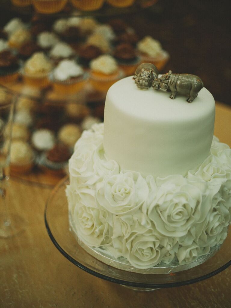 Silver hippo cake topper on a white floral wedding cake. 