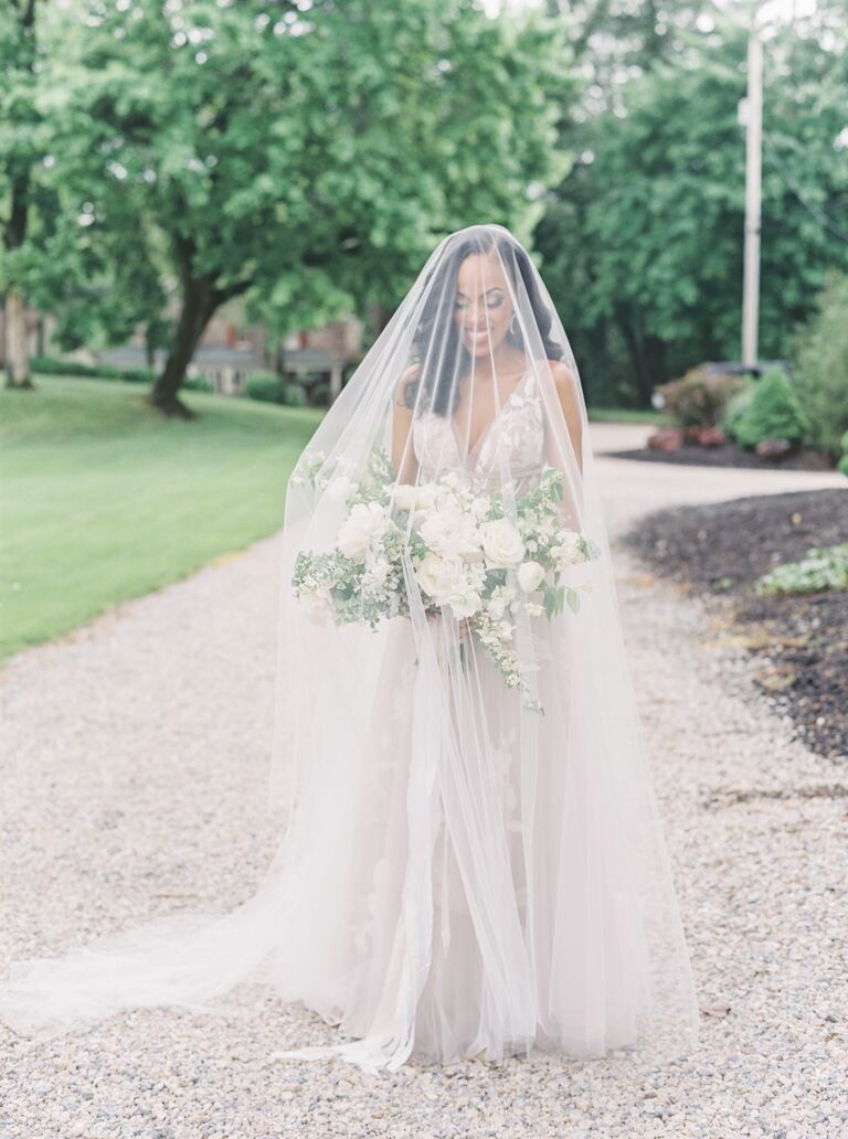 bride wearing pale purple tulle wedding ball gown stands outside at garden venue wearing sheer drop veil covering her face and upper body