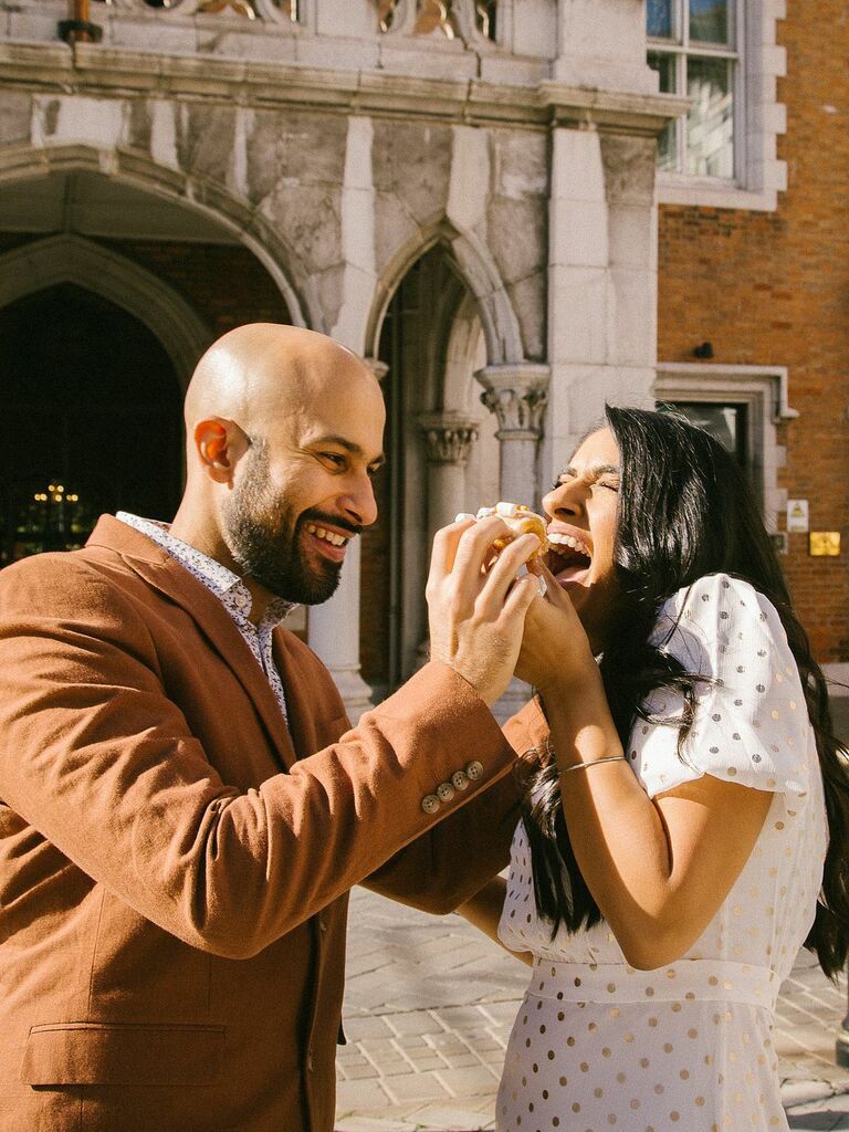 Couple laugh while eating donuts in the sunshine. 