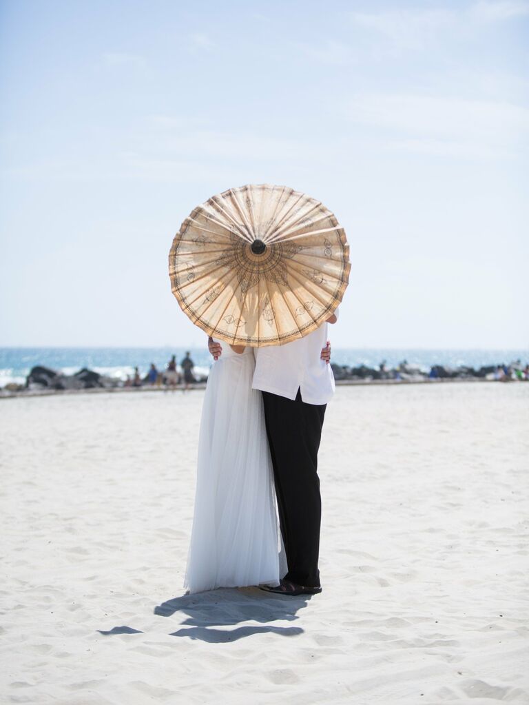 Couple embraces behind a stylish parasol. 