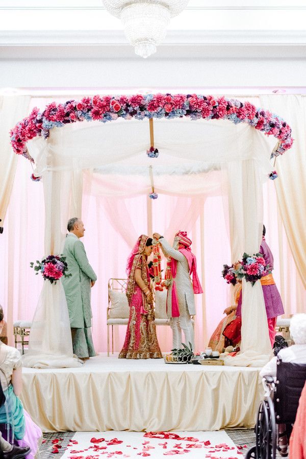 Couple underneath pink-and-white mandap in ballroom