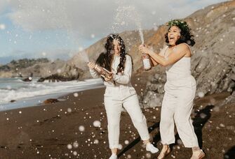 Couple pops champagne on the beach. 