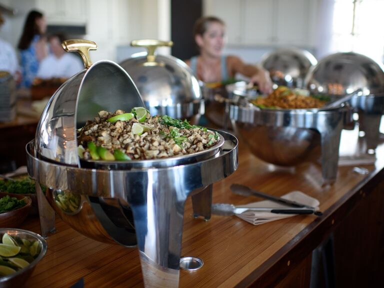 Buffet spread of taco fillings in silver serving vessels. 