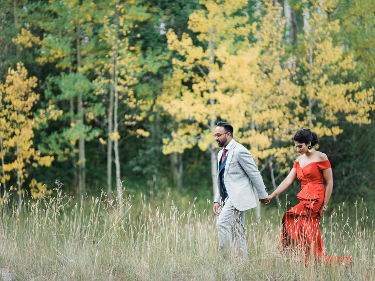 A groom and bride walk together through a meadow for their engagement photoshoot