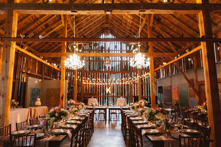 The reception took place in the Woodwalk Gallery’s spacious, historic barn, a rustic space that provided the couple with a blank canvas to make their own. Using a color palette of petal pink, mint and gold, the pair transformed the venue into the picture of glamour and elegance. Sequin-studded table runners, mercury glass accents, gilded cutlery and glitter-flecked chargers added a refined edge to the room, while fluffy arrangements of peonies, flickering candlelight and whimsical script table numbers filled the room with romance and life.rn