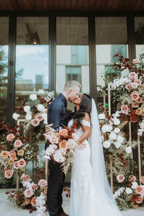 Groom and Bride in Off-the-Shoulder Gown Kiss, Floral Structures and Bouquet in Fall Colors