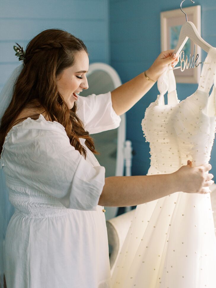 A bride getting ready and admiring her tea-length, vintage, thrifted wedding dress with pearl details.