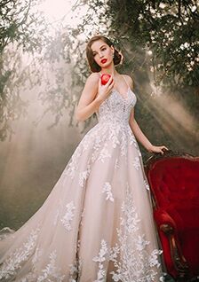 Brunette woman in the forest wearing a Snow White-inspired Allure Disney Fairy Tale Weddings dress and holding an apple.