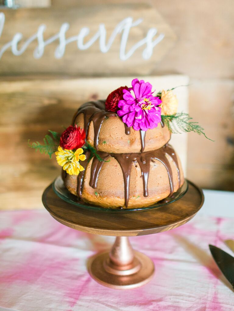 two tier bundt cake with chocolate drip glaze and purple, red and yellow flowers