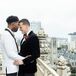 Grooms in White Jacket and Black Velvet Jacket Embracing on Balcony Overlooking San Francisco