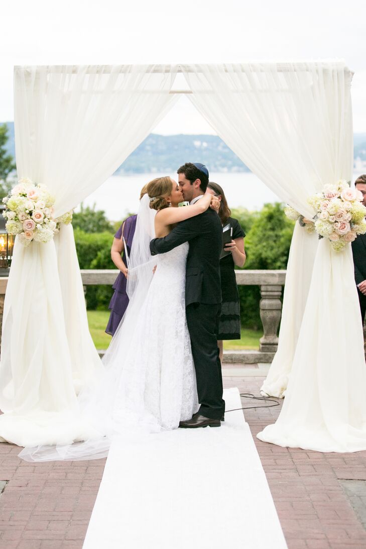 The newlyweds share a sweet first kiss under a fabric-draped chuppah in a ceremony overlooking the Hudson River in New York.