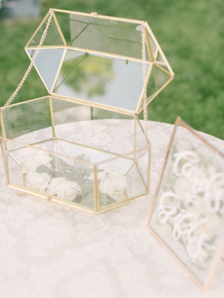 glass wedding card box with gold trim on top of white lace tablecloth