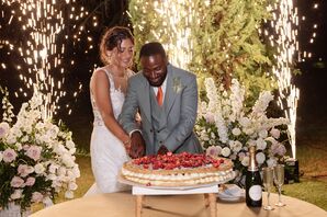 Bride in Fitted Gown, Groom in Teal Suit Cutting Large Cake, Sparklers in Background