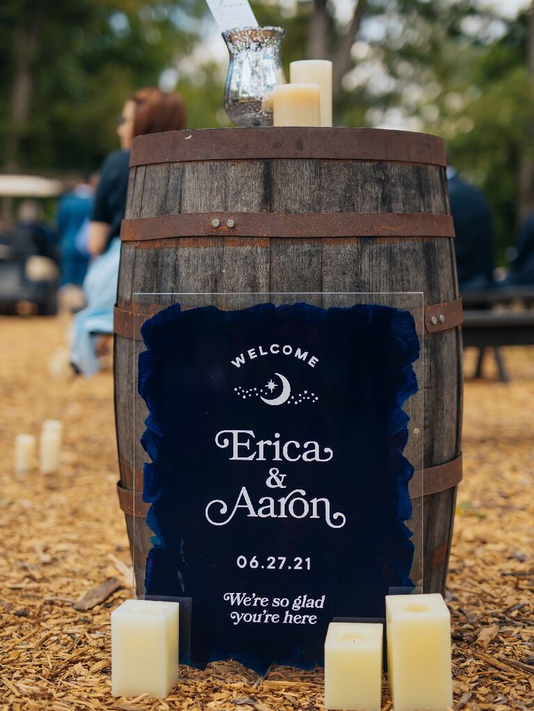 Dark blue celestial wedding welcome sign against barrel at outdoor barn wedding
