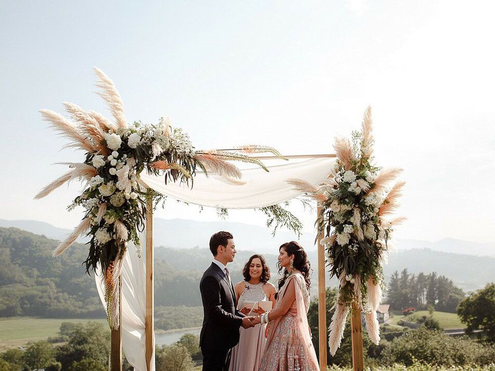 Couple exchanging vows in front of boho floral arch at outdoor summer wedding