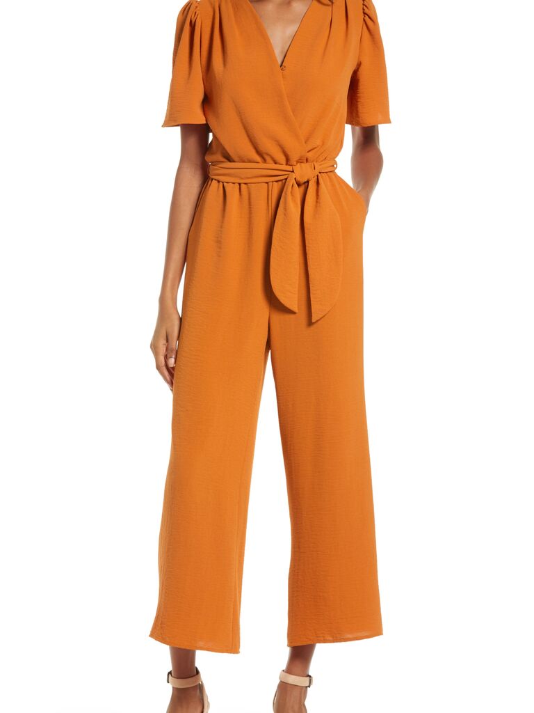 Model is wearing a rust jumpsuit with sleeves and a belt around the waist.