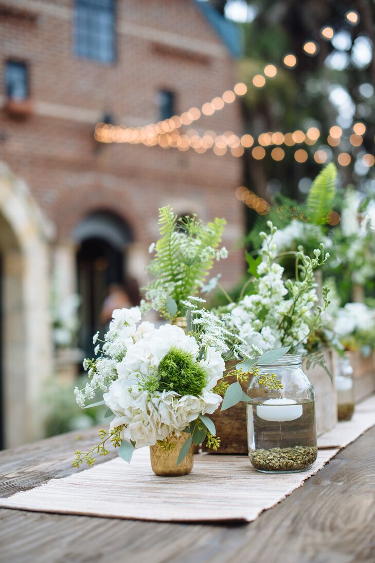 Soft white flowers and lots of wispy greenery freshened up the wooden reception tables, while complementing the wedding's natural setting. Floating candles place in mason jars worked with the strings of bistro lights to create a warm, inviting ambiance.