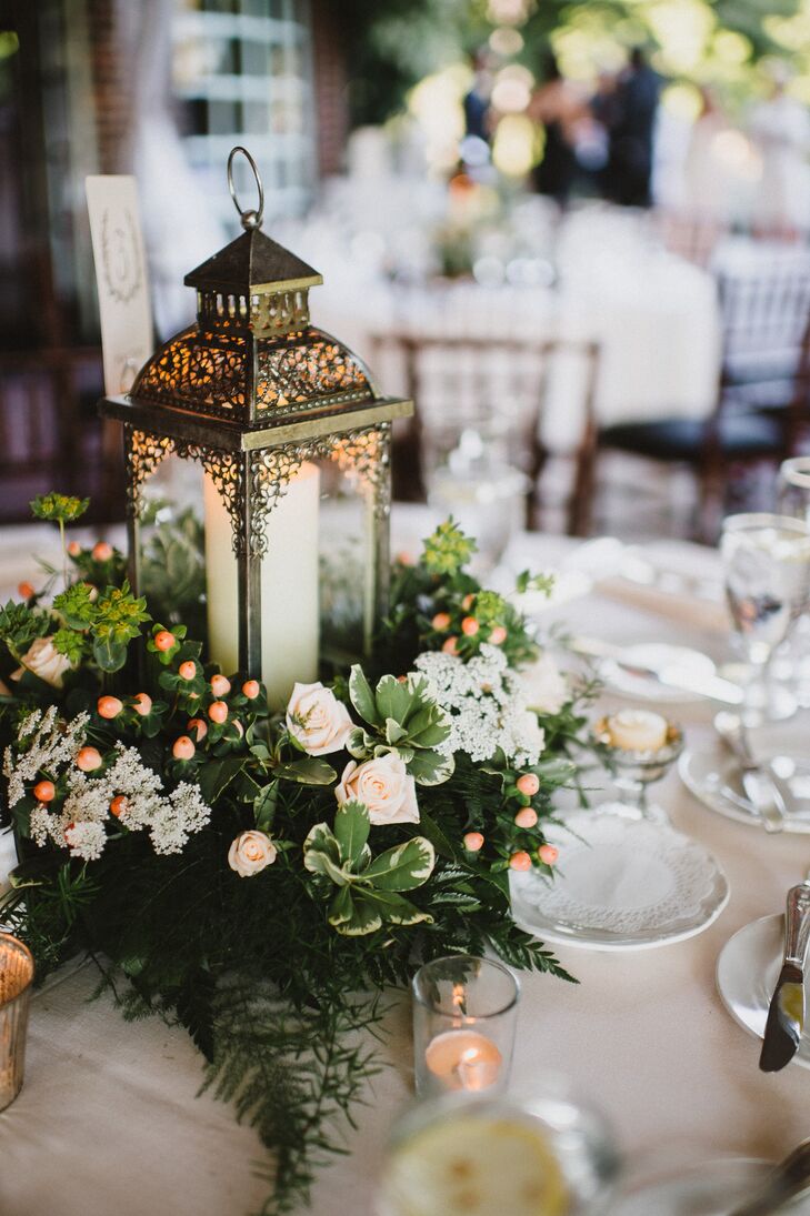 Reception centerpieces featured vintage pewter lanterns surrounded by a ring of greens and peonies with peach berries and votive candles.