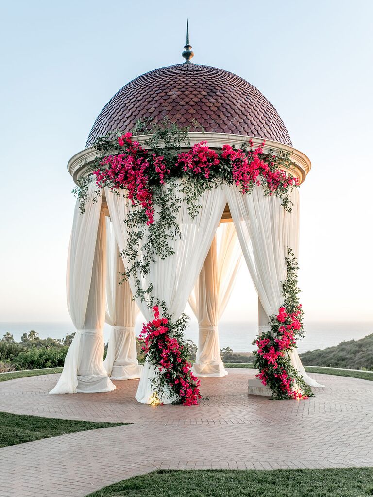 outdoor wedding ceremony pavilion decorated with white drapery and pink bougainvillea