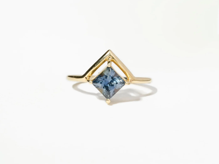 A square teal sapphire in a geometric gold band.