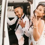 Couple smiles at camera and shows off their new wedding rings standing in front of white jeep