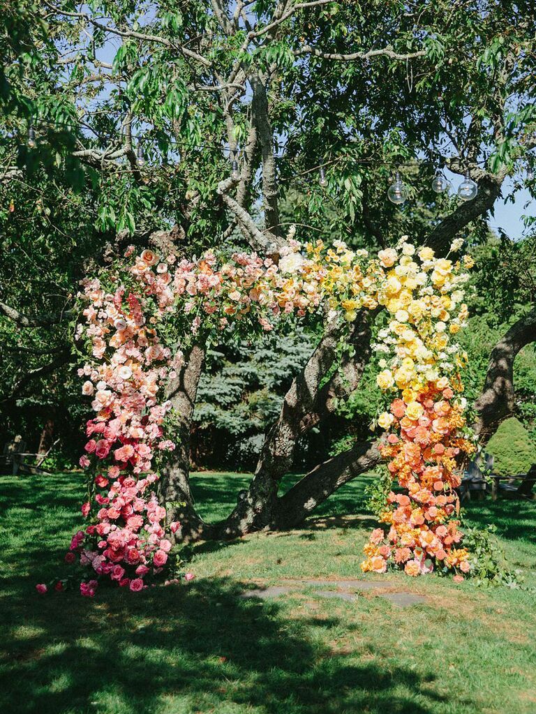 Pink ombré statement floral arch at outdoor summer wedding ceremony