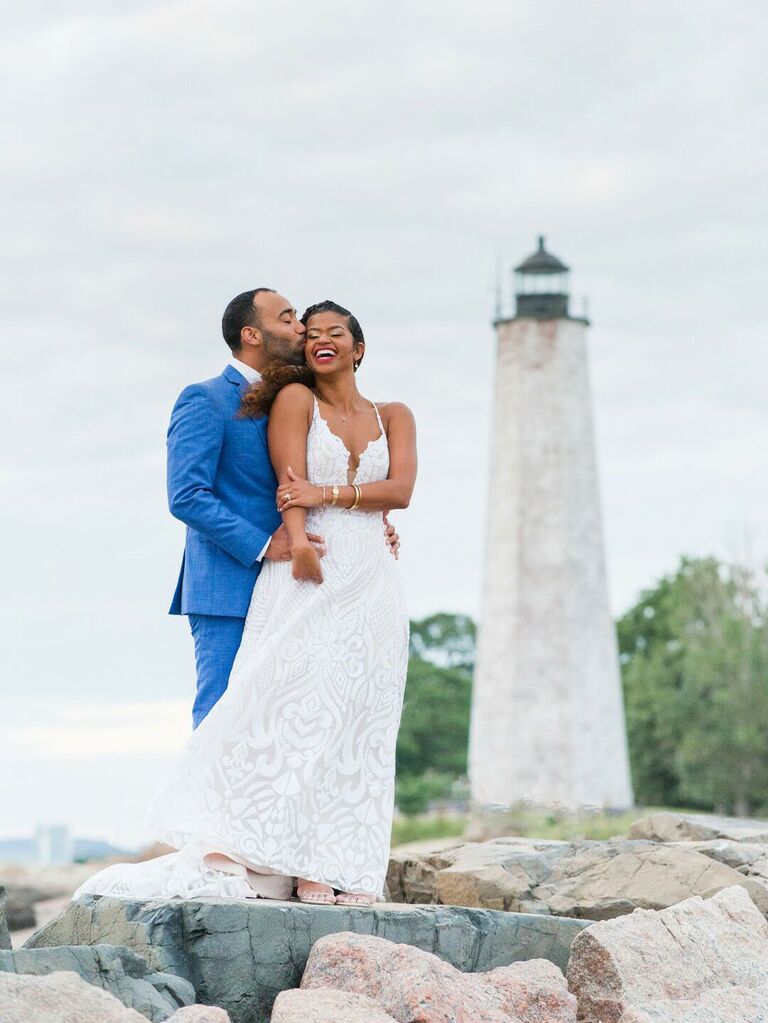 Bride and groom posing for portraits in front of lighthouse at nautical preppy summer wedding