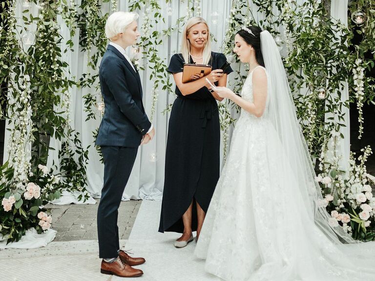 wedding officiant couple reading vows in front of flower wall