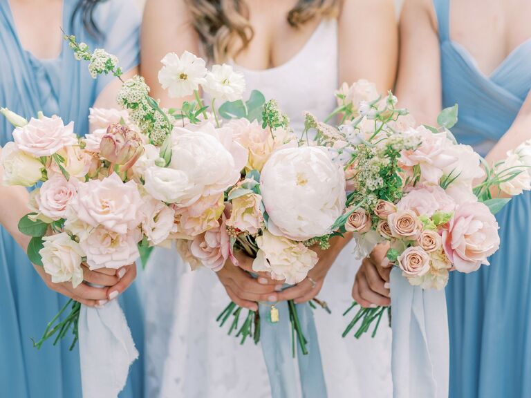 A bride and her bridesmaids hold pale white, pink, and yellow flowers.