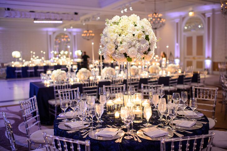 Add drama and texture to the formal ballroom, Lauren and Johnathan opted for a mix of square, round and long rectangular table shapes. The centerpieces reflected this variation, with round tables featuring bundles of romantic white blooms piled high on tall glass pedestals, while the rectangular and square tables were topped with low arrangements and a scattering of brightly lit candles.