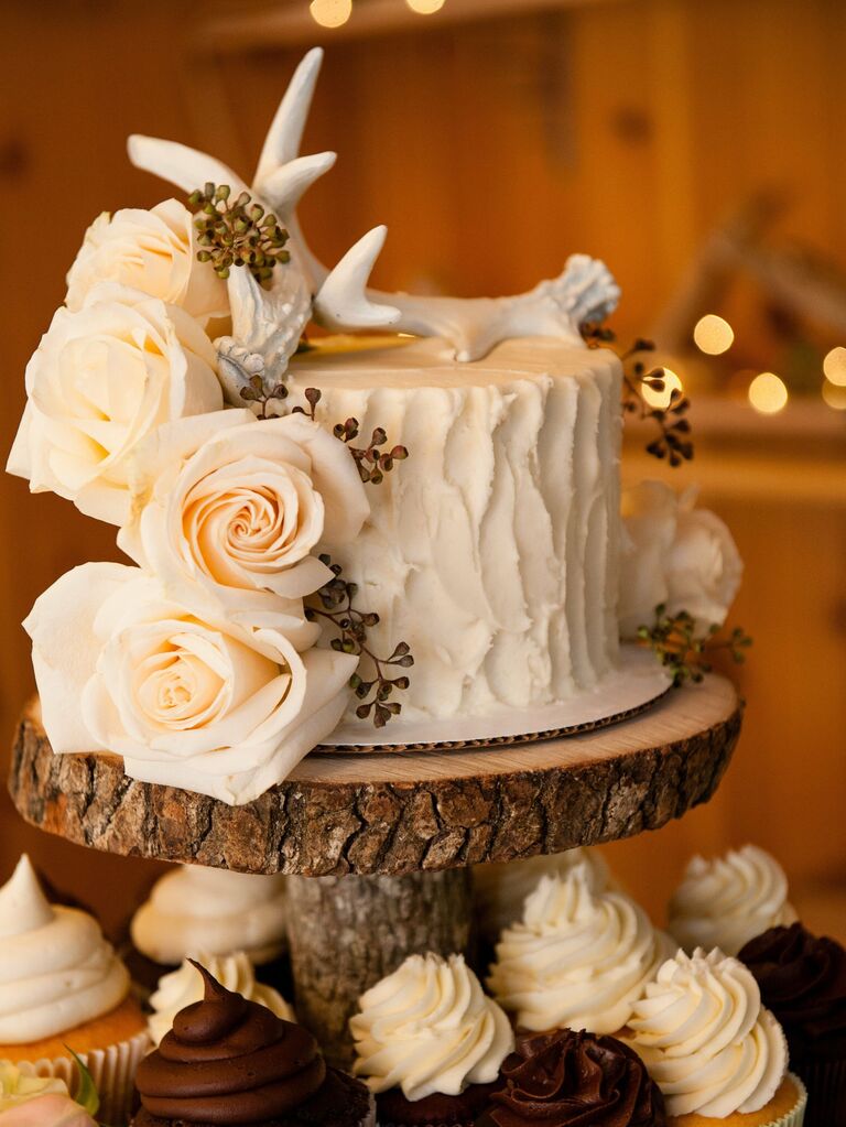 white buttercream one tier wedding cake on wooden tree stand with white roses and white antler topper