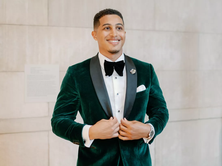 A groom smiles, wearing a vibrant autumnal-green velvet tuxedo jacket.