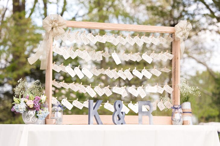 Their escort card display definitely brought in the country theme. Guests found their names attached to lines of twine in a wooden frame. Arrangements of baby’s breath, blush roses, lilacs and blue hydrangeas accented the base with a little down-home flair.