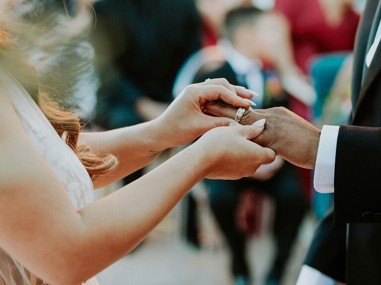 A bride places a wedding band on her new husband's finger.