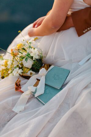 Natural Wildflower Bouquet and Blue Vow Booklets Laying on Bride's Gown