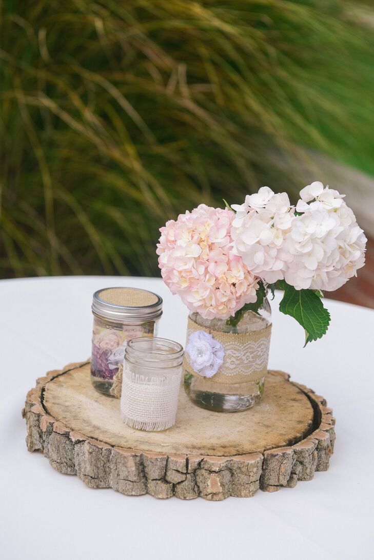 Pink and white hydrangeas were arranged in a mason jar alongside several others, positioned on a slab of wood.
