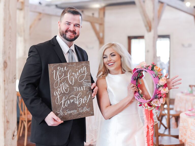 Groom holding sign and bride holding tambourine bouquet.