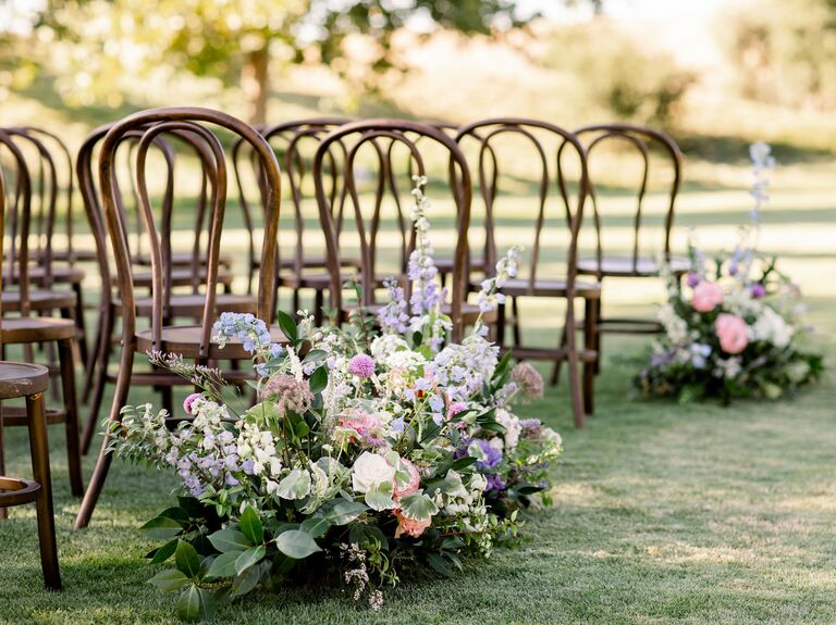 outdoor wedding ceremony aisle marker with blue and purple delphinium, pink peonies and greenery