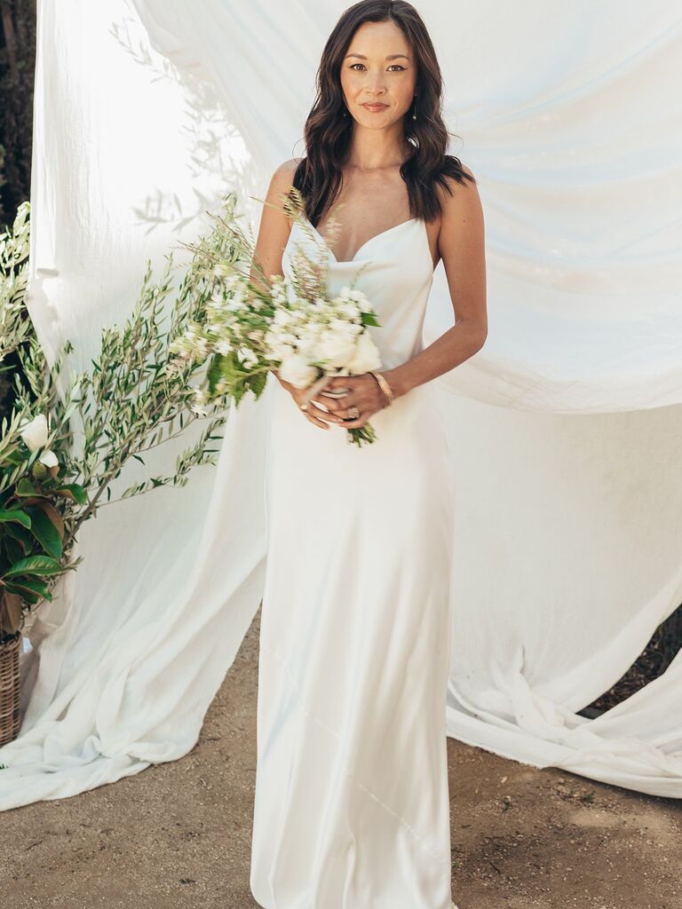 Model wears a white silk dress and holds a bouquet. 