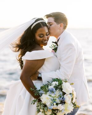 Couple in White, Suit and Wedding Dress, Kissing by the Ocean With Flowers