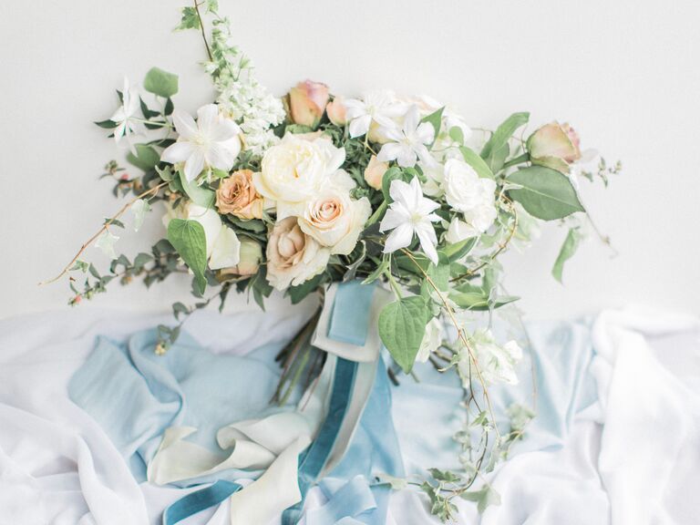garden-style wedding bouquet with white and peach flowers tied with light blue ribbons